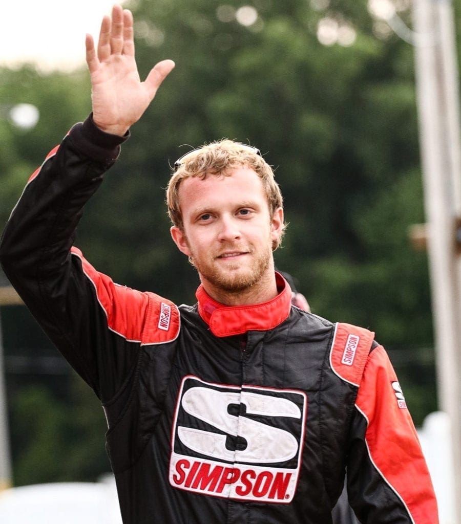 A race car driver in his first suit and waving to a crowd at a recent race.