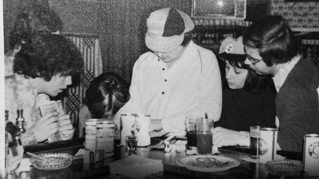 A group of men and women at a bar examining a spot sheet.