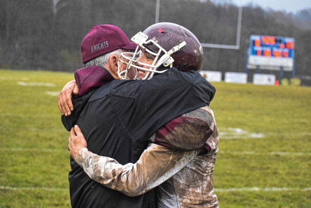 A head coach in high school football hugs one of his players.
