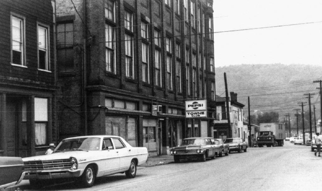 A photo of an older building with several cars along the street.