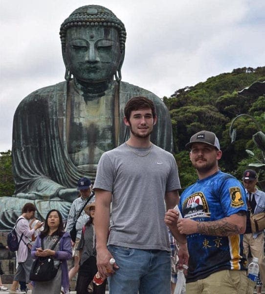 Two young men in front of a large Buddah.