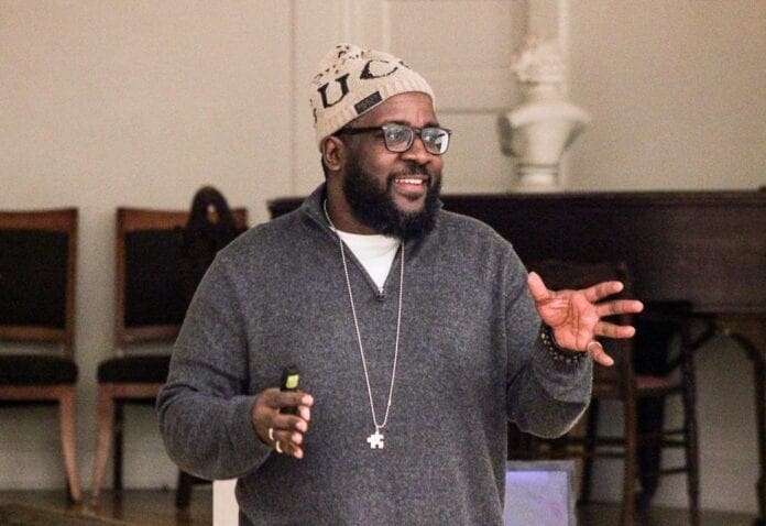 A black man speaking to a group of people.