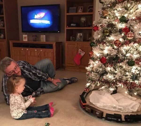 A grandfather with a grandkid near a Christmas tree.