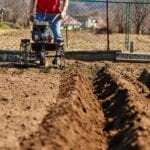 Gardener cultivate ground soil with tiller tractor or rototiller, cutivator